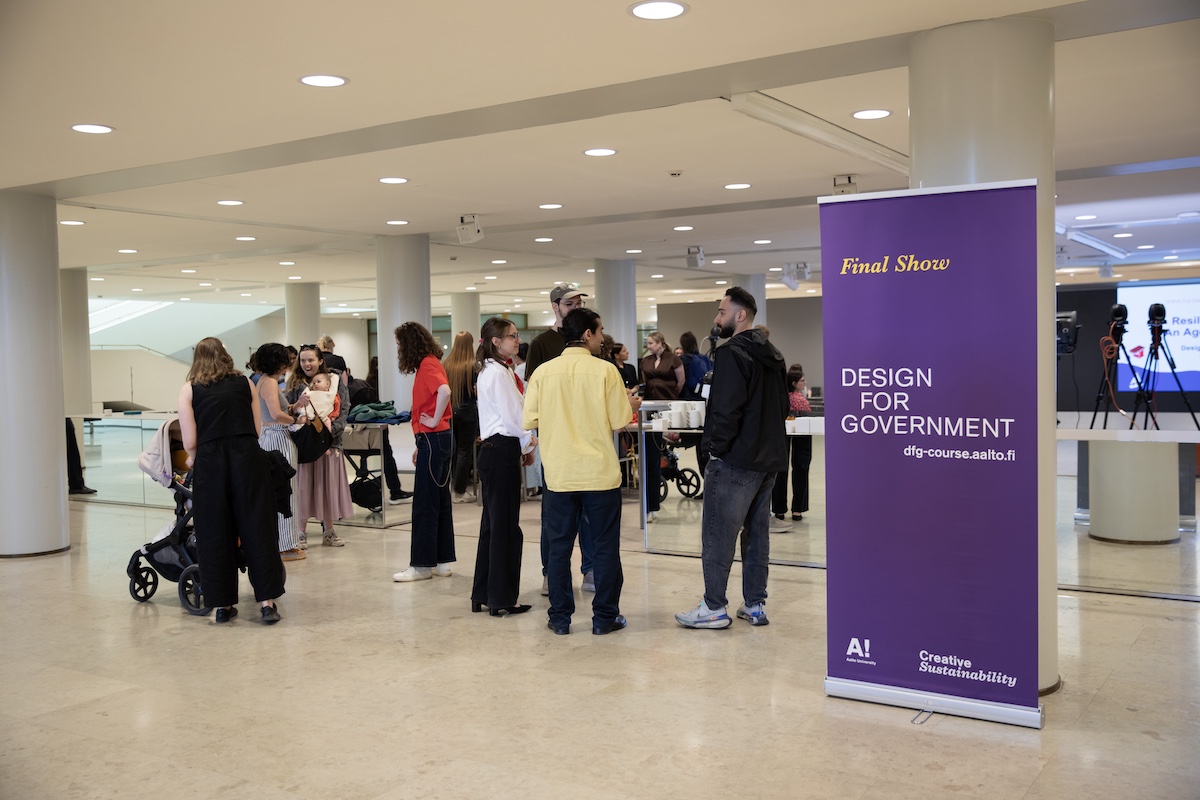 A group of people at an event and a Design for Government pull-up banner in violet next to them