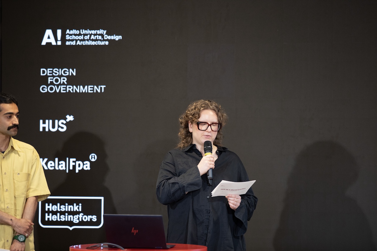 A person in black clothing holding a microphone and notes