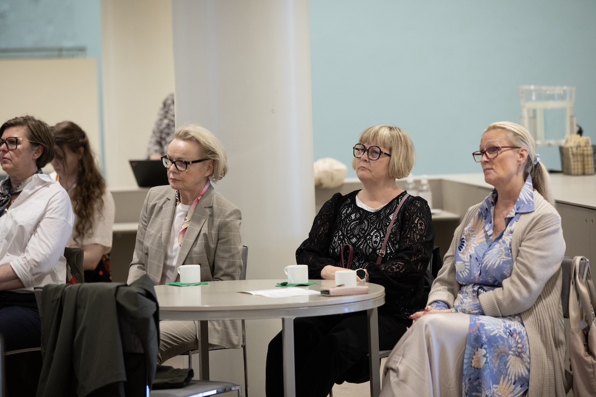 Three audience members around a table with cups watching the presentation