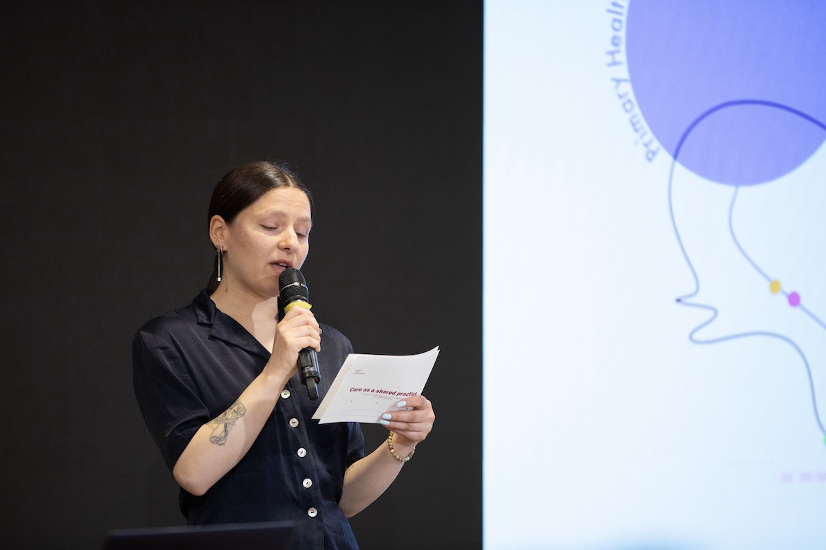 A person presenting in dark clothing holding a microphone and notes